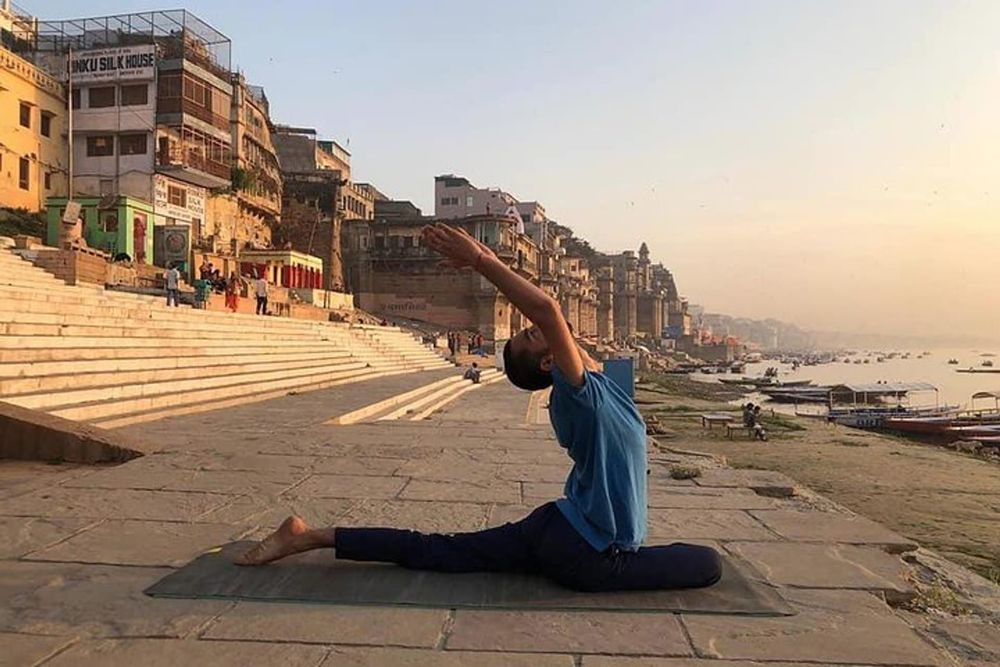 Traveler practising a yoga posture at sunrise near the Ganges River in Varanasi